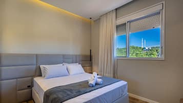 A modern hotel room with a large bed, a view of a tower, and a window with blinds.