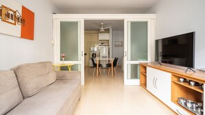 A modern living room with a sofa, a dining table with chairs, a TV, and a kitchen area visible through an open door. - Well Equipped apt in BC Center 300m fr/ sea Ecp055 (Balneário Camboriú)