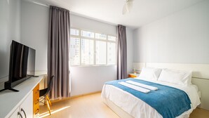 A hotel room with a bed, a desk with a TV, a chair, and a window with curtains. - Well Equipped apt in BC Center 300m fr/ sea Ecp055 (Balneário Camboriú)