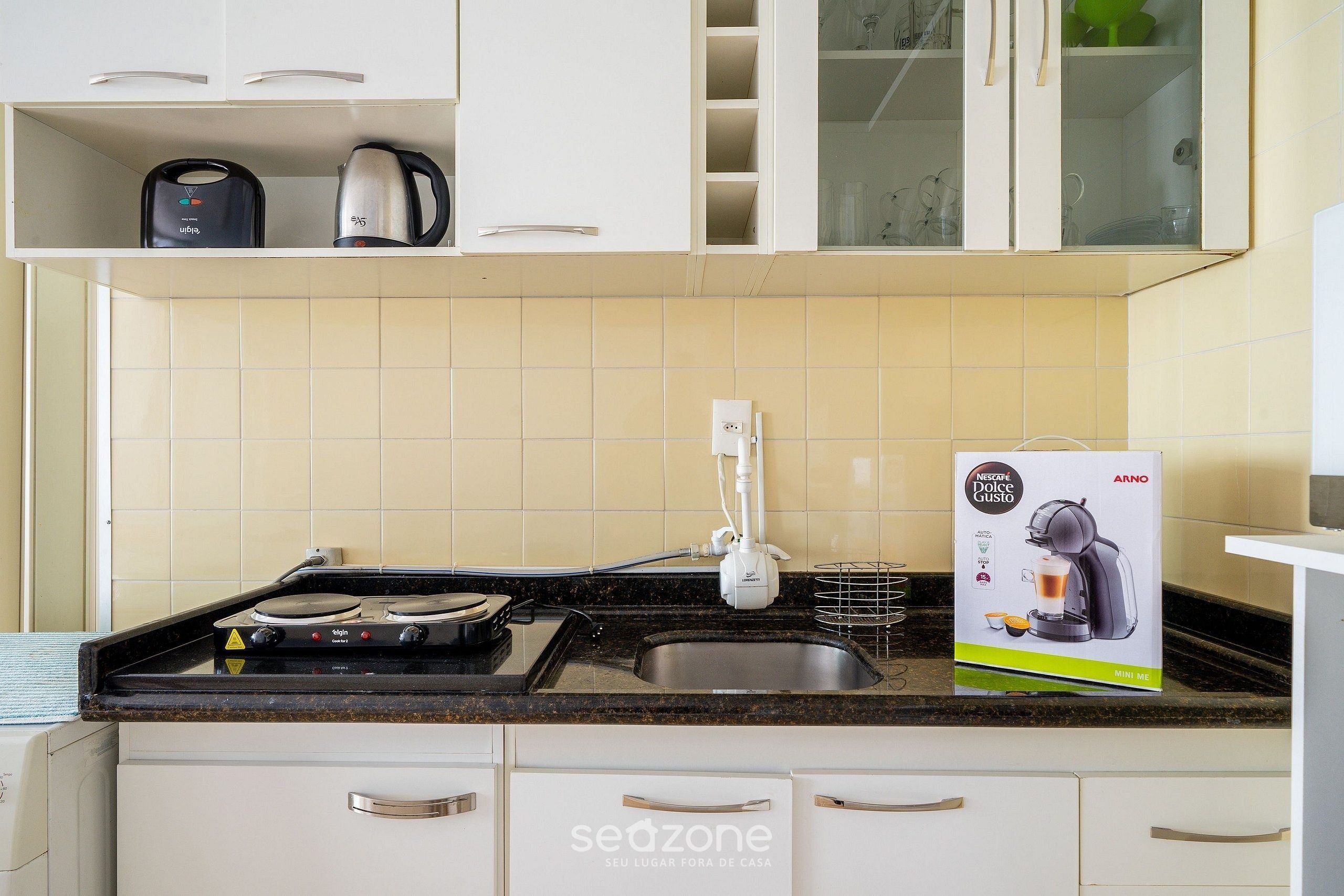 A kitchen with a stove, kettle, and a coffee machine box.