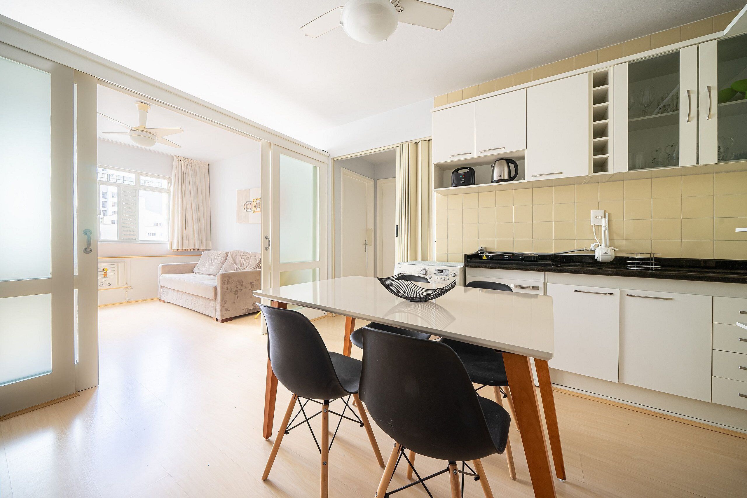 Cozinha moderna com armários brancos, uma mesa de jantar com cadeiras pretas e um ventilador de teto.