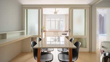 Uma área de refeições com uma mesa grande e cadeiras, um ventilador de teto e vista para o exterior através de grandes janelas.