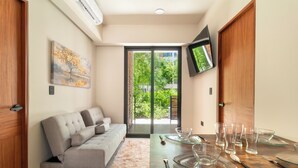 Una sala de estar moderna con un sofá, una mesa de comedor con vasos de vidrio transparente y un televisor montado en la pared.