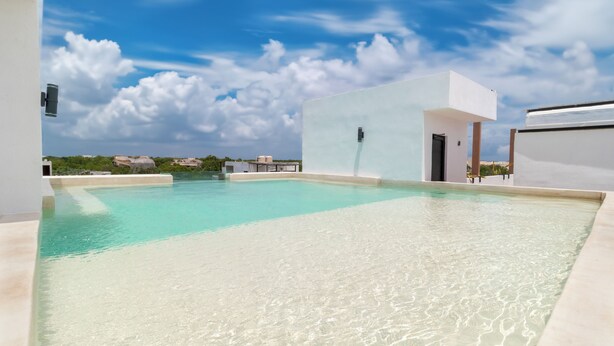 Una piscina en la azotea con agua cristalina, rodeada de arquitectura moderna y un cielo despejado.