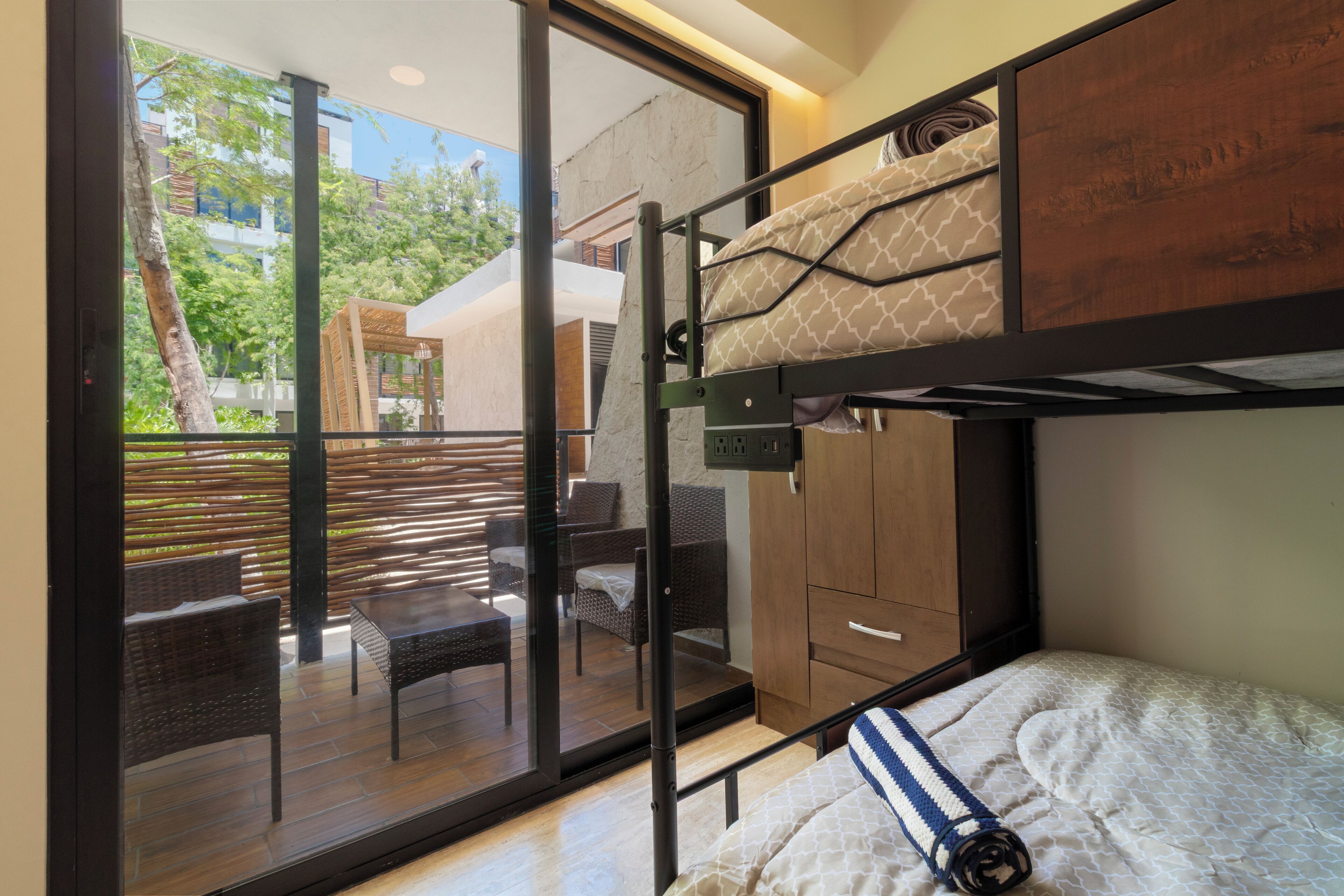 A modern room with a bunk bed, a glass door leading to an outdoor seating area, and a wooden cabinet.