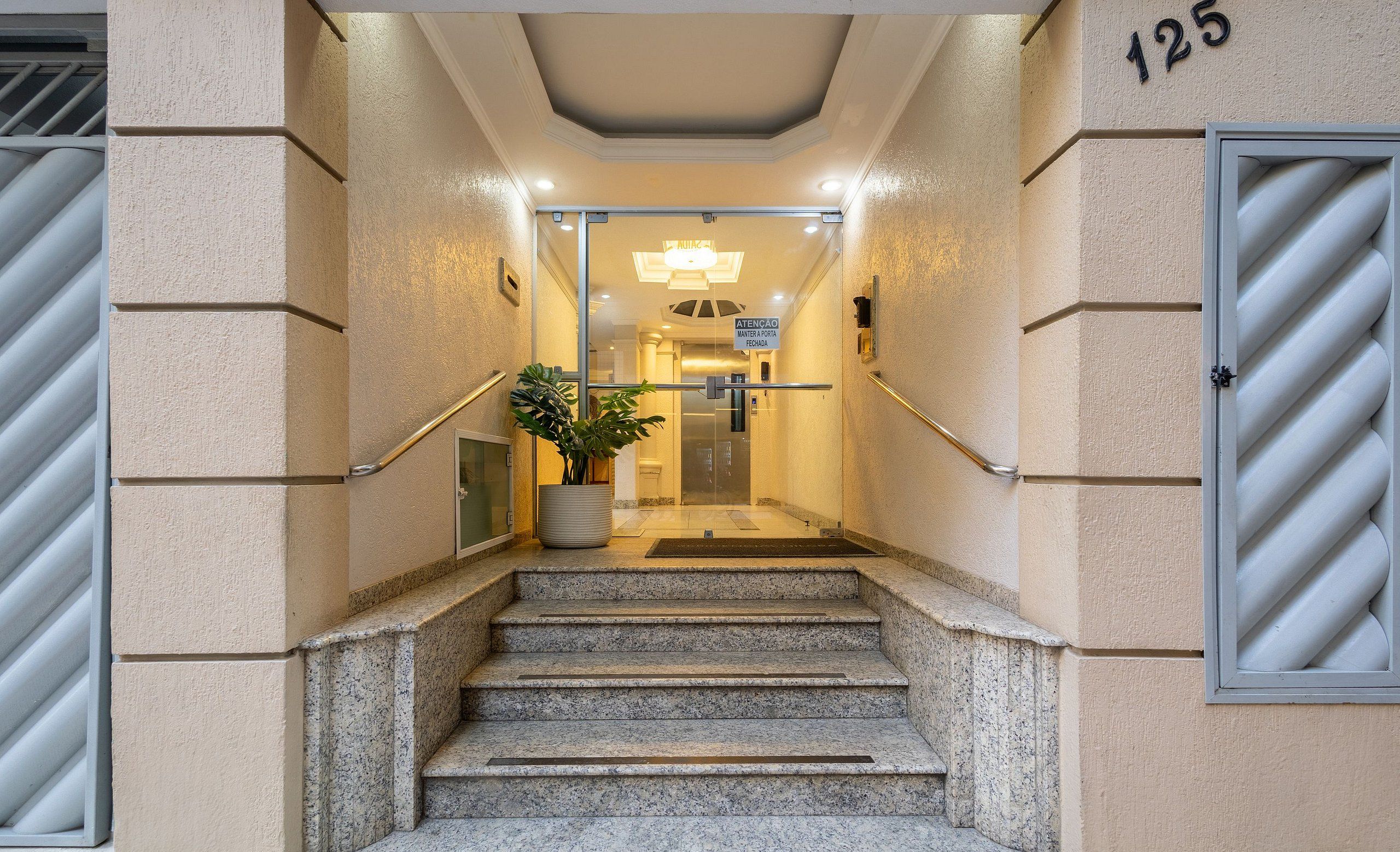 A hotel entrance with a staircase leading to the lobby, a potted plant, and a sign indicating the entrance.