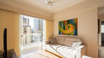 A modern living room with a sofa, a TV, and a large window with a view of buildings.