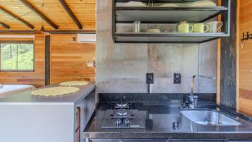 Eine moderne Küche mit einer Granitarbeitsplatte, Spülbecken aus Edelstahl und einem eingebauten Backofen. Über der Spüle befindet sich ein Regal mit Geschirr und eine Topfhalterung.