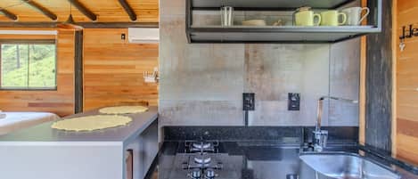 A modern kitchen with a granite countertop, stainless steel sink, and a built-in oven. There is a shelf above the sink holding dishes and a hanging pot rack.