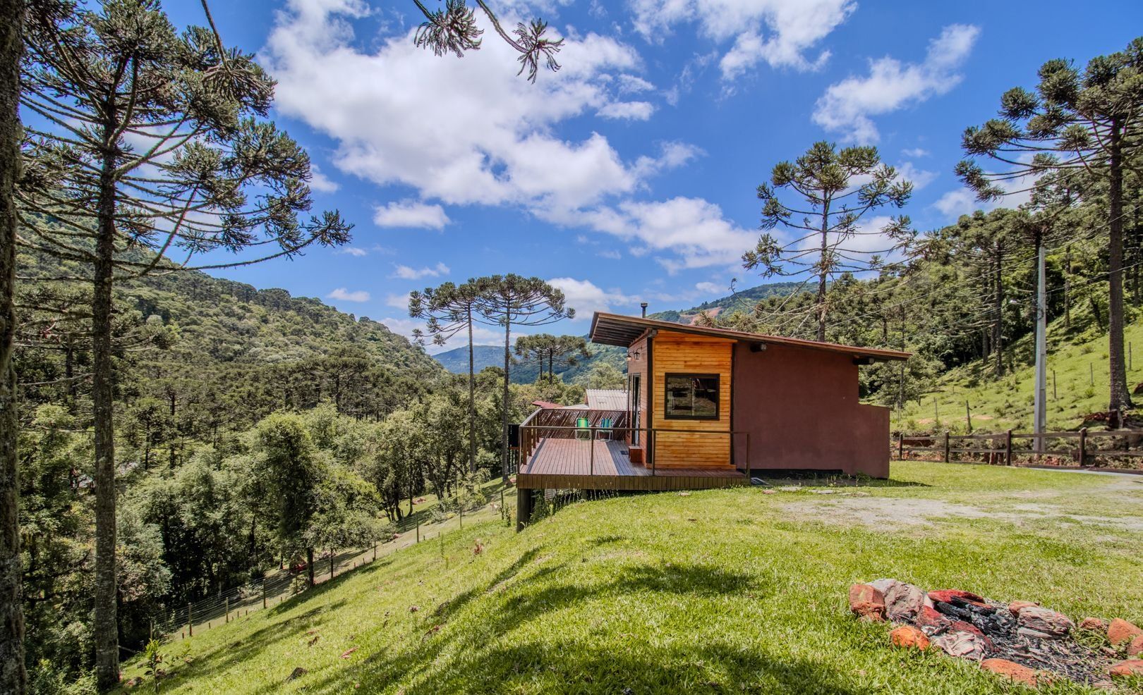 A cabin with a wooden deck, surrounded by a forested hillside.