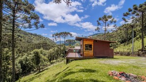 Uma cabana com um deck de madeira, rodeada por um morro arborizado.