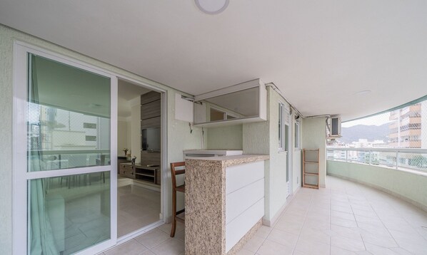 Un balcon doté d’un coin cuisine, comprenant un plan de travail et des placards, ainsi qu’une porte-fenêtre coulissante donnant sur un espace intérieur.