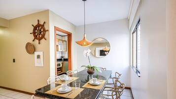 A dining area with a marble table, white chairs, a ship's wheel decoration, a hanging light fixture, and a mirror on the wall.
