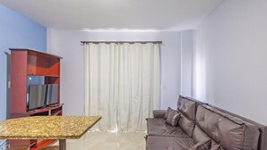 A living room with a brown leather sofa, a TV on a stand, a dining table with chairs, and a curtain. - Beachfront Apartment in BC Great Location Eit302 (Balneário Camboriú)