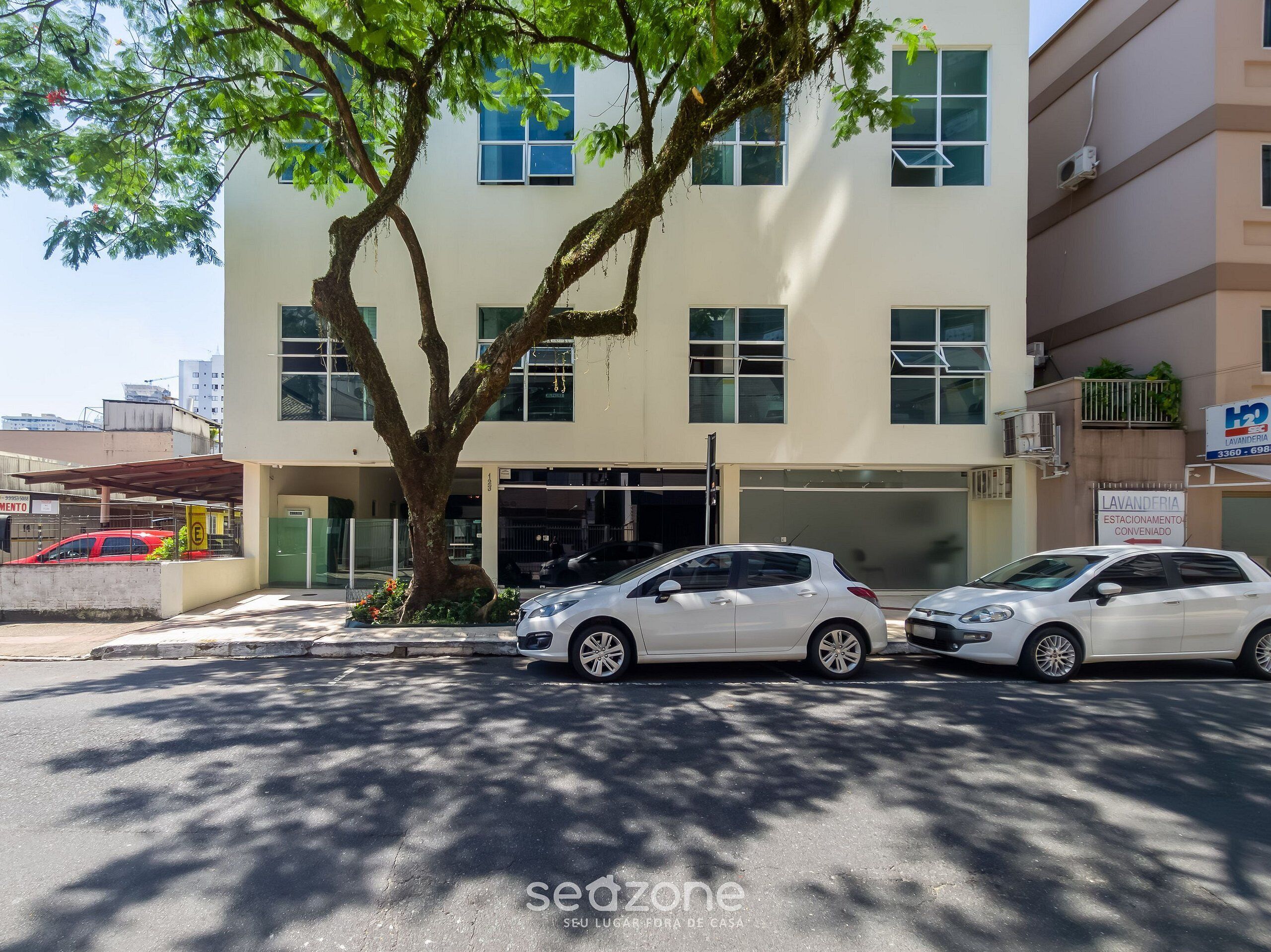 Un edificio con dos coches aparcados delante, un árbol y un cartel de lavandería.