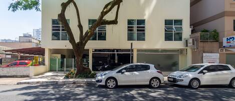 Un edificio con dos coches aparcados delante, un árbol y un cartel de lavandería.