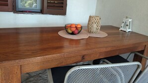 Una mesa de madera con un tapete tejido, un cuenco de fruta, un jarrón tejido y un pequeño farol blanco.