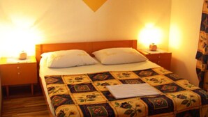 A hotel room with a bed, two bedside tables, a nightstand, a wall-mounted picture, and a patterned bedspread. - Apartments A&N Pakoštane - Two Bedroom Apartment with Sea View (A2) (Pakoštane)