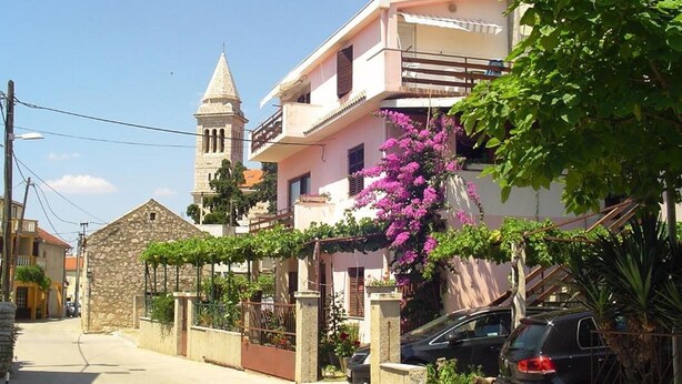 A residential street with a stone building, a pink house with a balcony, and a church tower. - Apartments A&N Pakoštane - Two Bedroom Apartment with Sea View (A2) (Pakoštane)