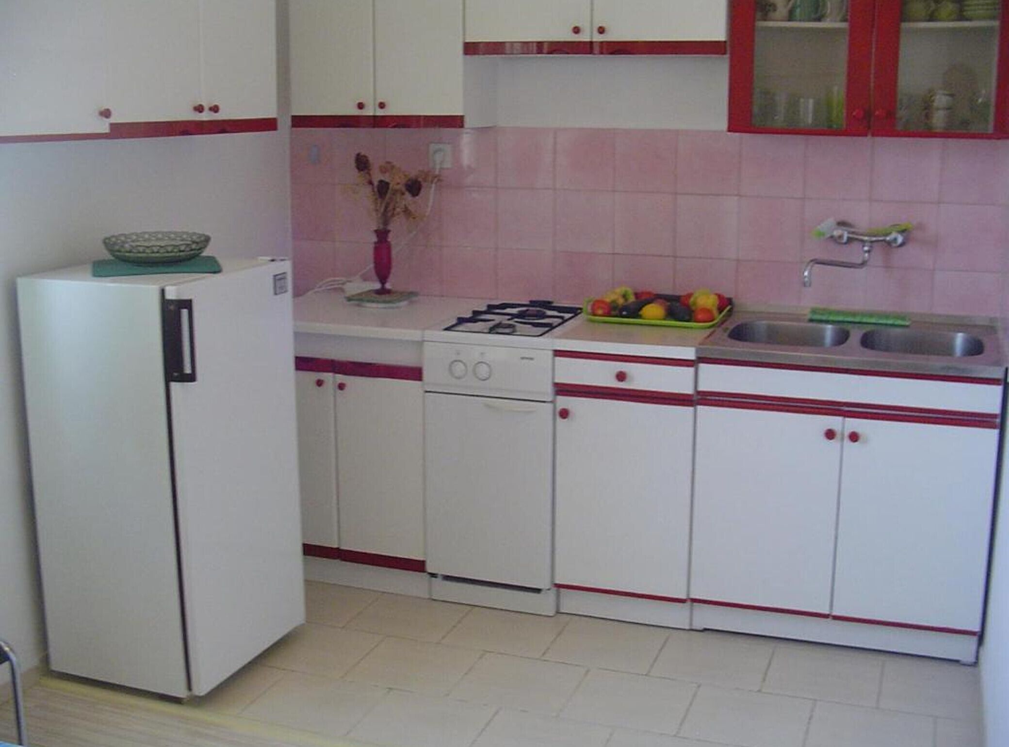A compact kitchen with white cabinets, a refrigerator, a stove, and a sink.