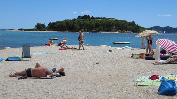 A beach with people sunbathing and swimming, a boat in the water, and a hill with trees in the background. - Apartments A&N Pakoštane - Two Bedroom Apartment with Terrace (A3) (Pakoštane)