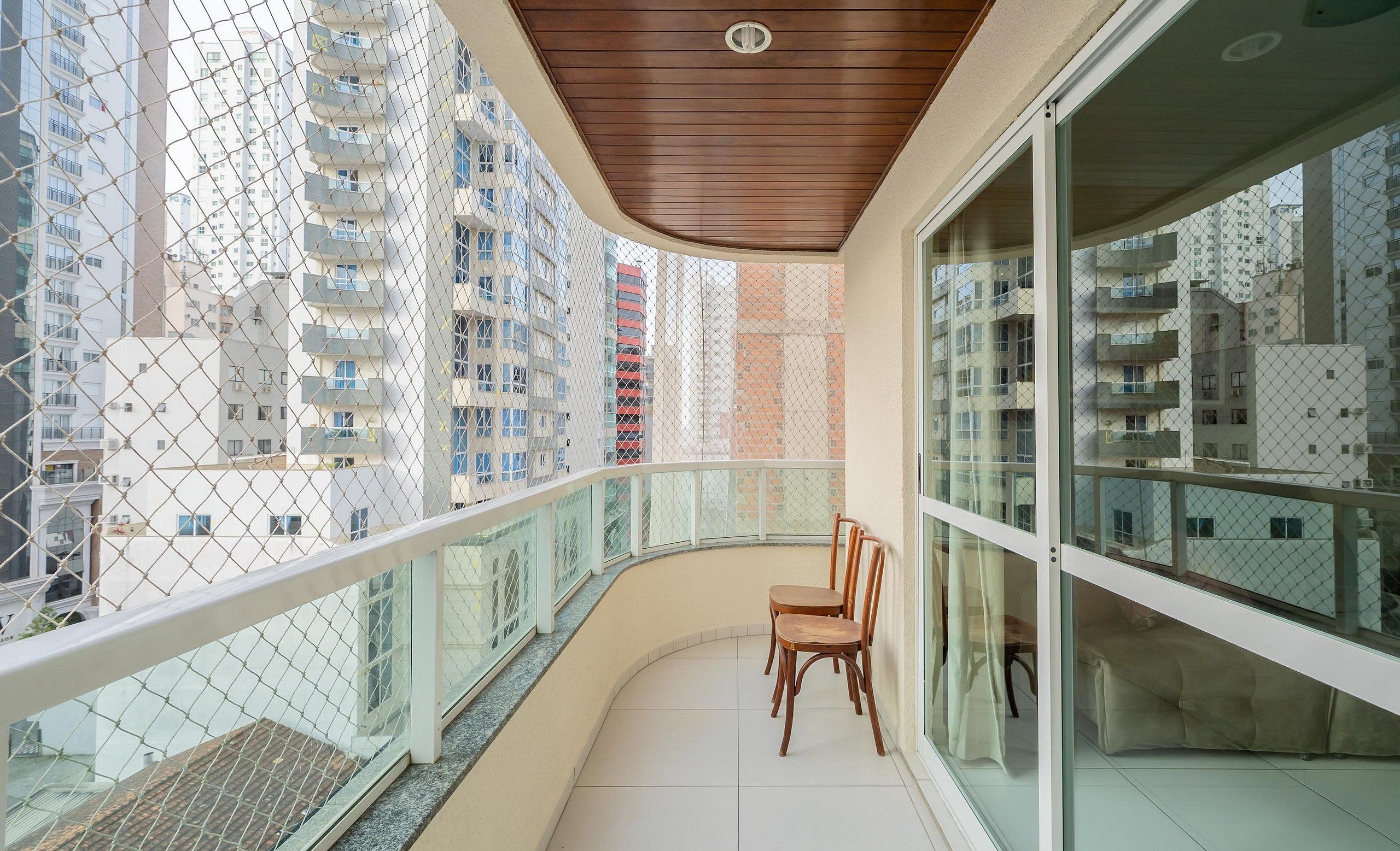 A balcony with a wooden ceiling, glass railings, and a view of high-rise buildings.