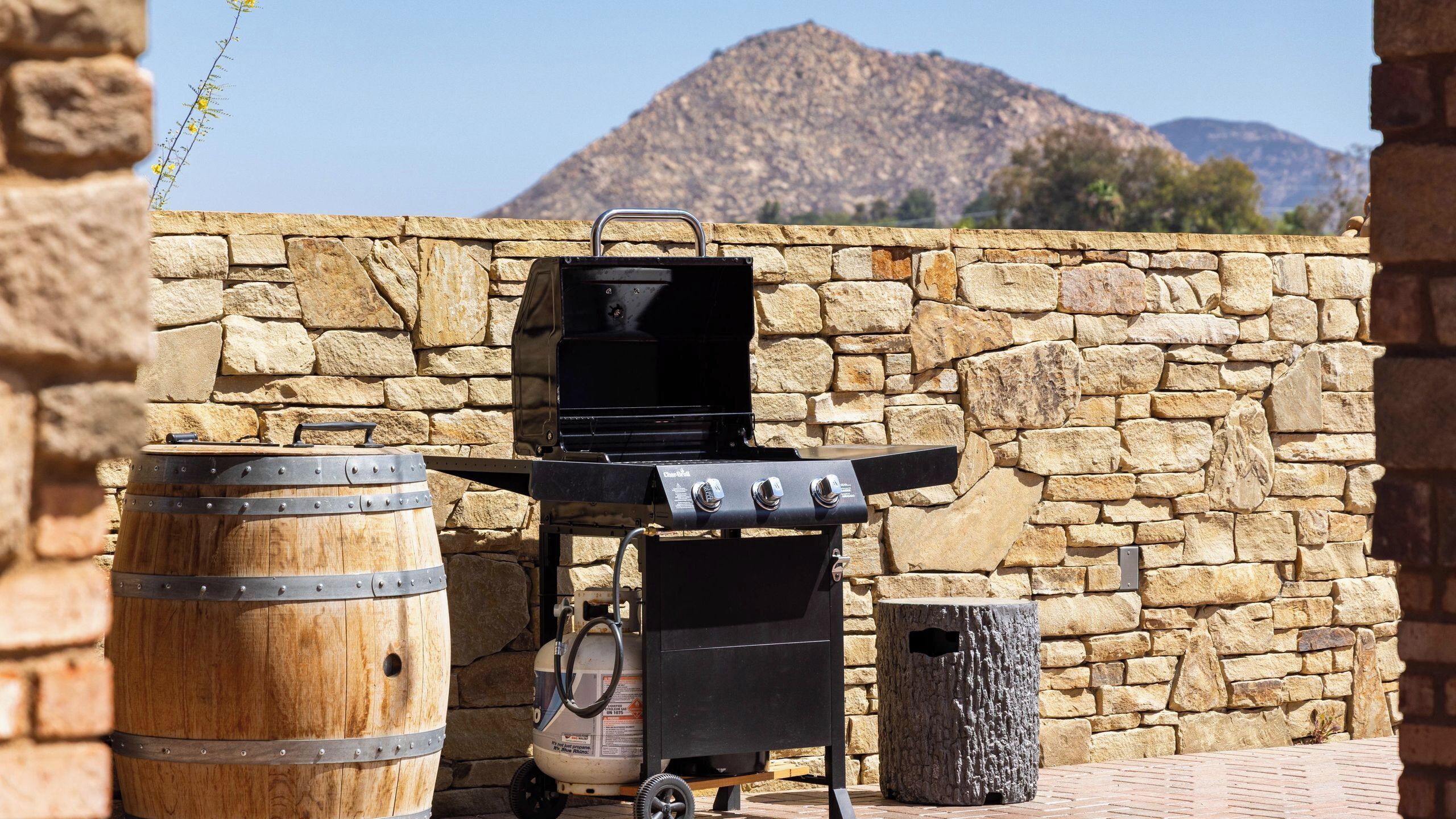 A barbecue grill with a stone wall backdrop and a mountain in the distance.