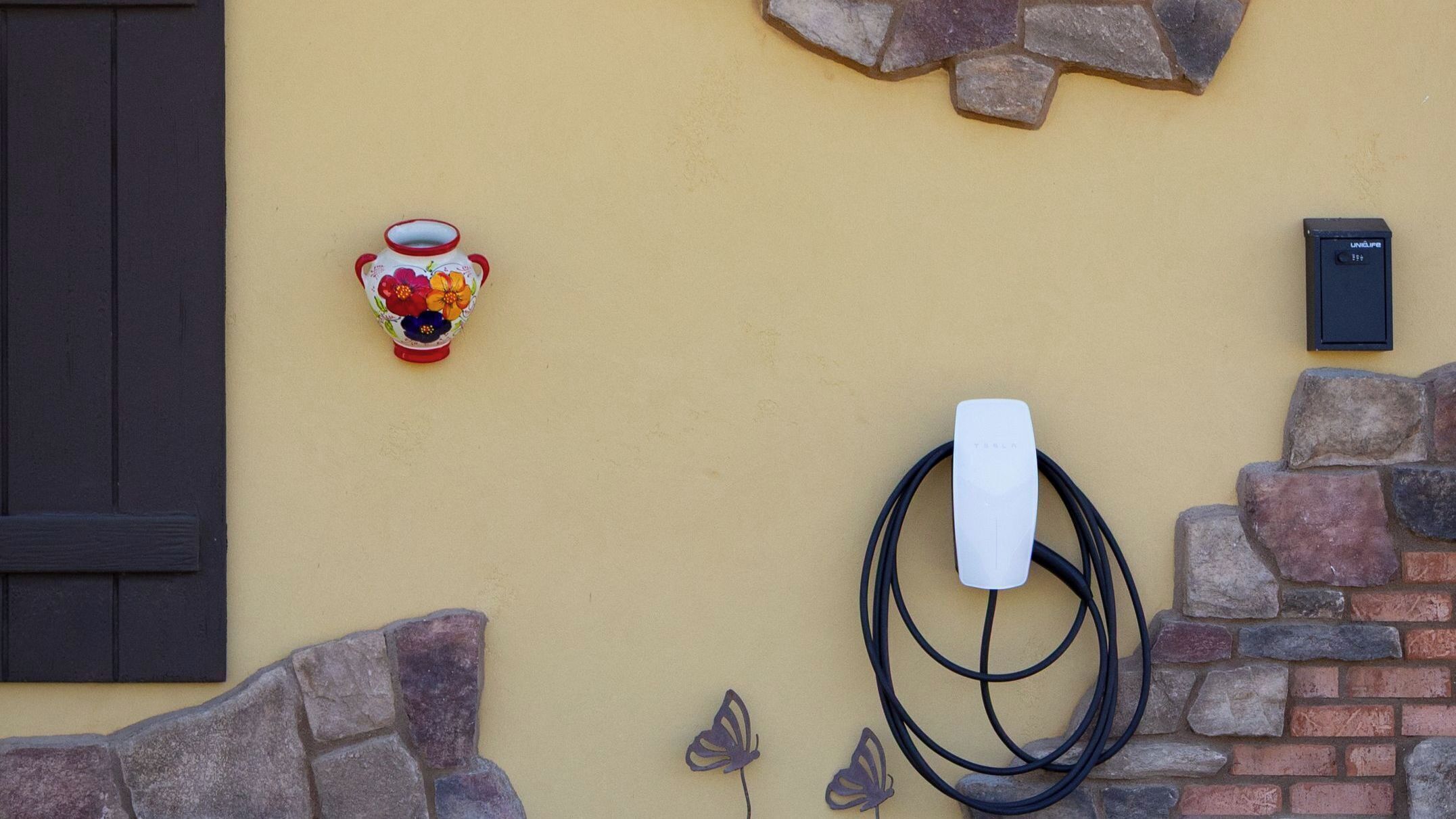 A wall-mounted Tesla charging station with a decorative vase and a small box on the wall.