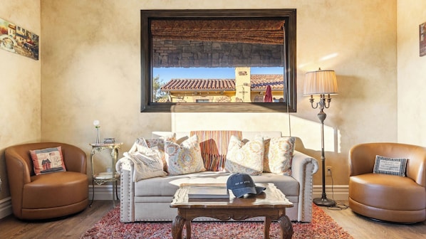 A living room with a sofa, two armchairs, a coffee table, a lamp, and a window with a view of buildings. - Soaking Tub, Vineyard Views & Wine Trail Access The Casita at Vines Estate by Avantstay (Temecula)