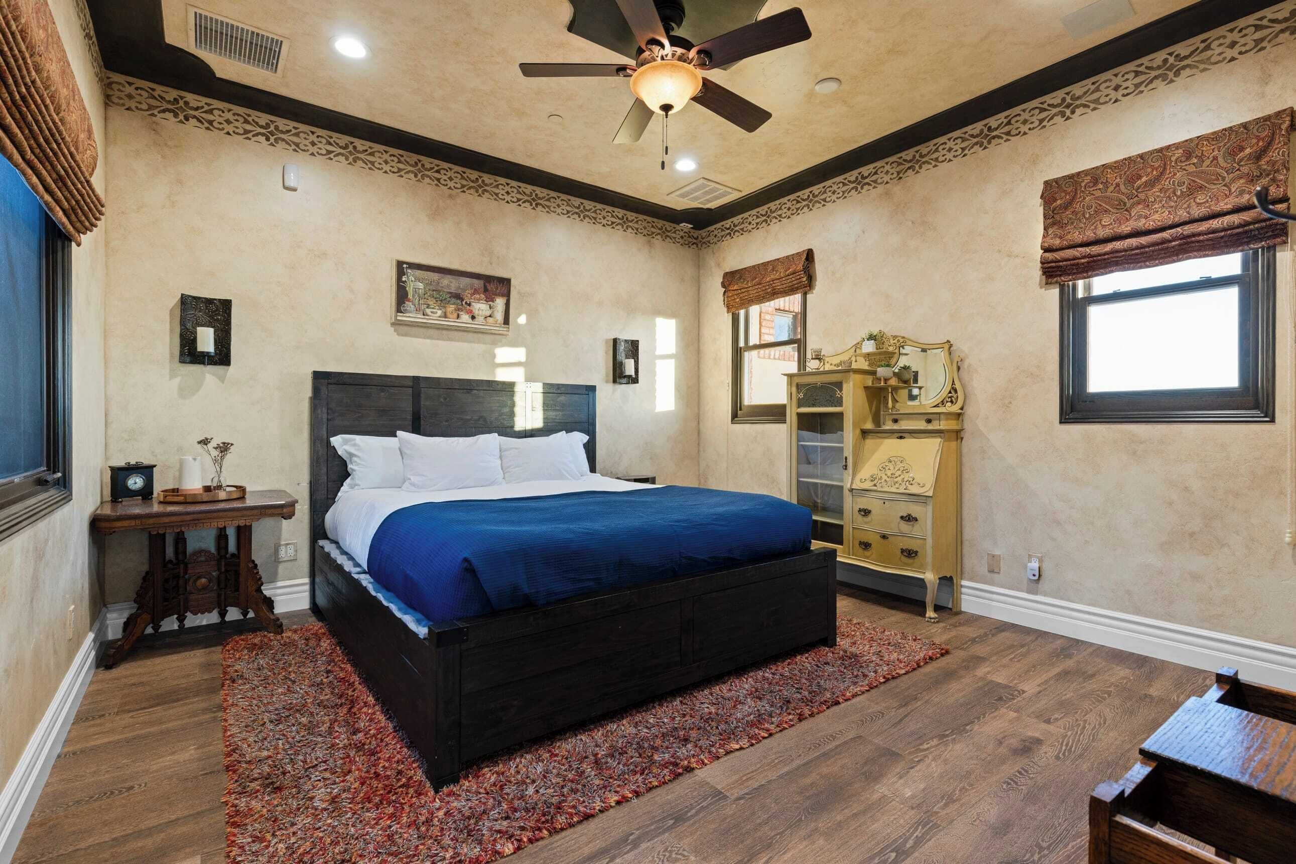 A bedroom with a large bed, a ceiling fan, a dresser, and a window with a valance.