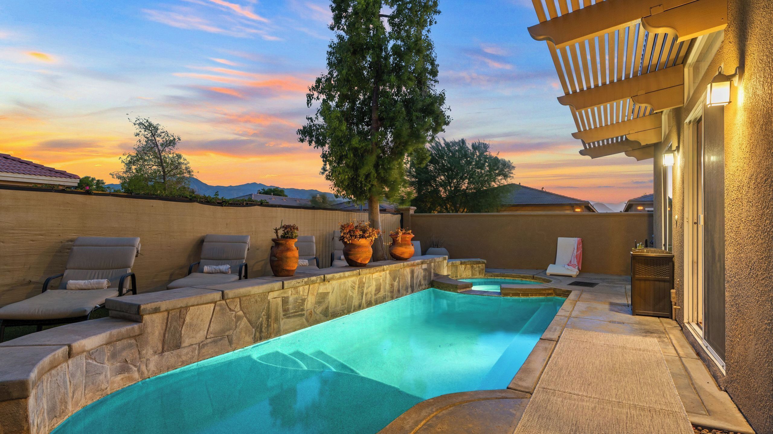 A swimming pool with lounge chairs, potted plants, and a pergola with lights.