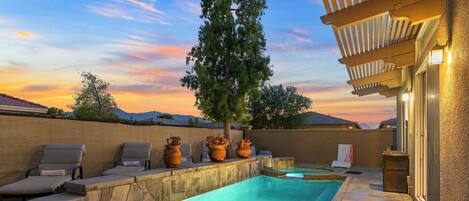 A swimming pool with lounge chairs, potted plants, and a pergola with lights.