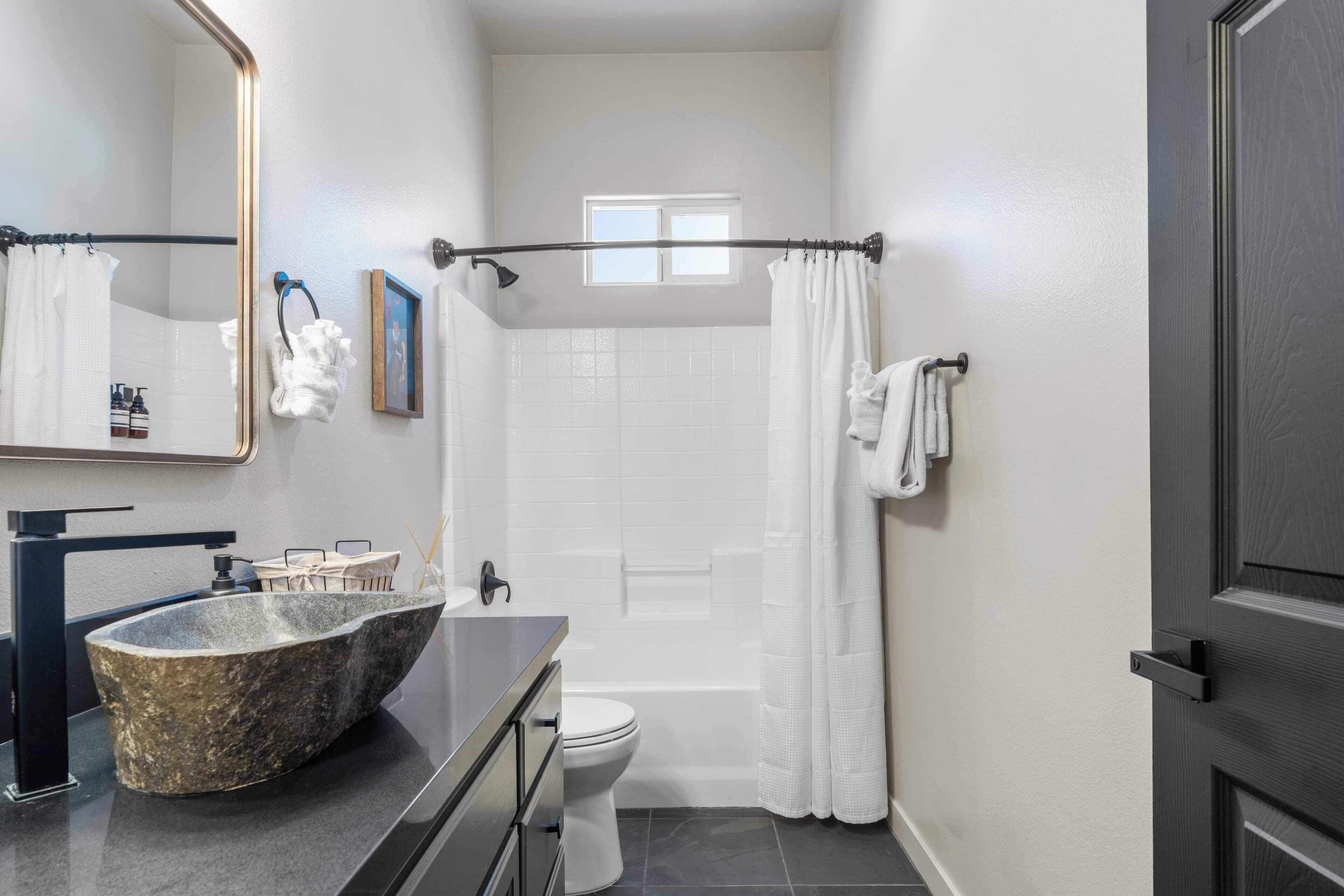 Une salle de bain moderne avec un lavabo en pierre, un robinet noir, des toilettes blanches et un rideau de douche.
