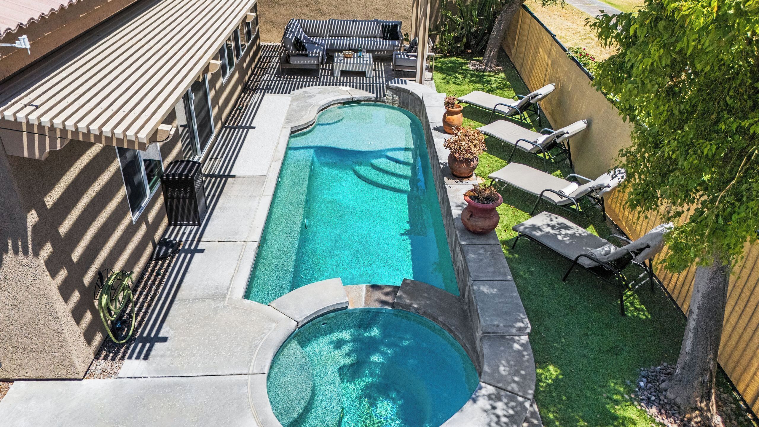 Une piscine dotée d’une terrasse ensoleillée, de chaises longues et d’un petit jacuzzi.