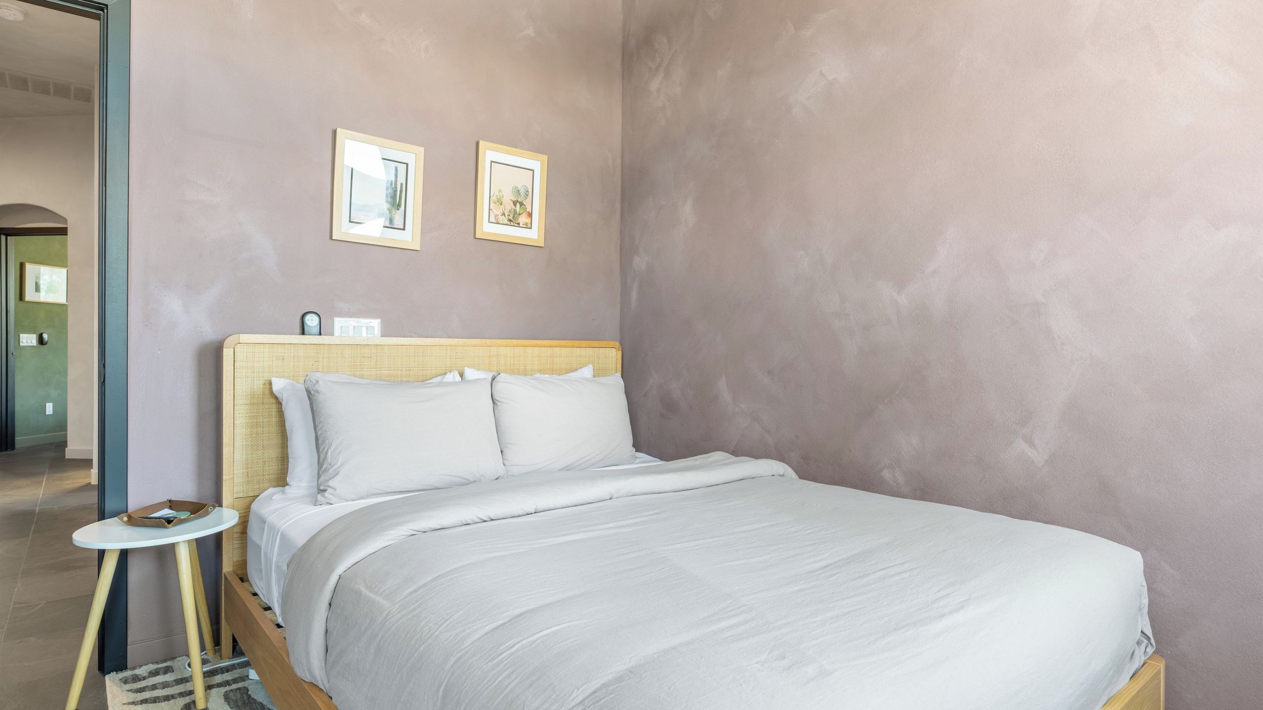 Un dormitorio con una cama, una mesita de noche, un reloj de pared y dos cuadros enmarcados.
