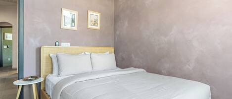 Un dormitorio con una cama, una mesita de noche, un reloj de pared y dos cuadros enmarcados.