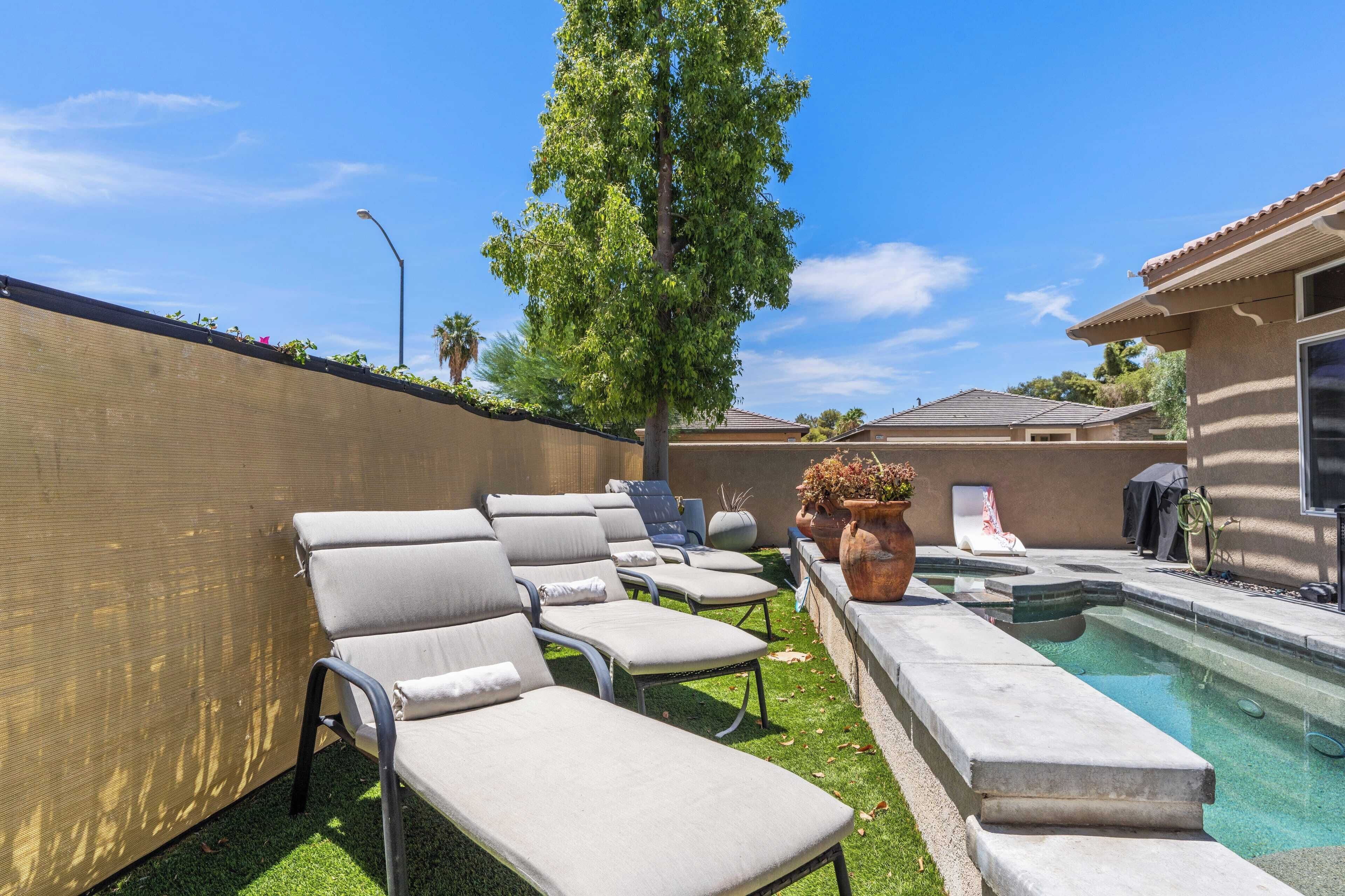 A pool area with lounge chairs, a tree, and a building in the background.