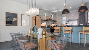 A modern kitchen with a central island, pendant lights, and a dining area with wire mesh chairs. - Designer Desert Oasis w/ Pool, Hot Tub, Outdoor Lounge The Riley by Avantstay (Indio)