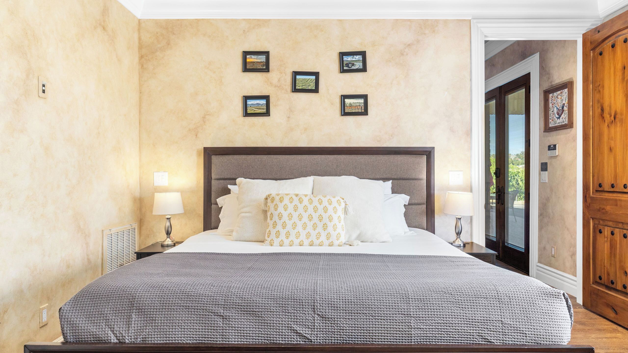 A hotel room with a large bed, two bedside lamps, a headboard, and a wall with framed pictures.