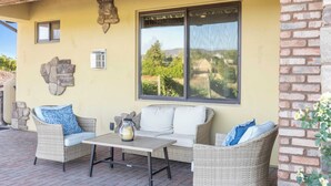 Une terrasse extérieure aménagée avec des meubles en osier, une table et une vue sur un vignoble, visible à travers de grandes fenêtres.