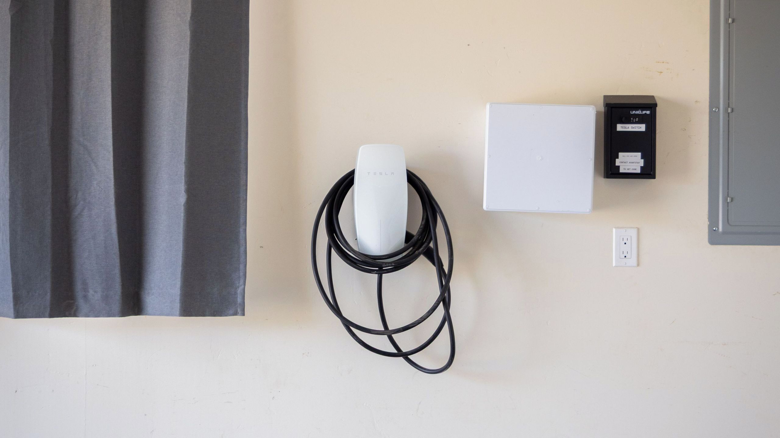 Een Tesla laadstation met een witte doos en een zwart apparaat aan de muur.