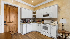 A kitchen with white cabinets, a wooden door, a microwave, a stove, and a small table with a lamp. - New-build Temecula Villa With King Suite, Patio & Vineyard Views The Villa by Avantstay (Temecula)