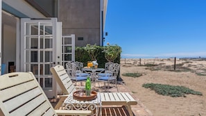 An outdoor seating area with tables and chairs, a glass of juice, and a view of the beach. - Oceanfront Home Walk to Balboa Pier + Scenic Views Balboa Peninsula Point by Avantstay (Newport Beach)