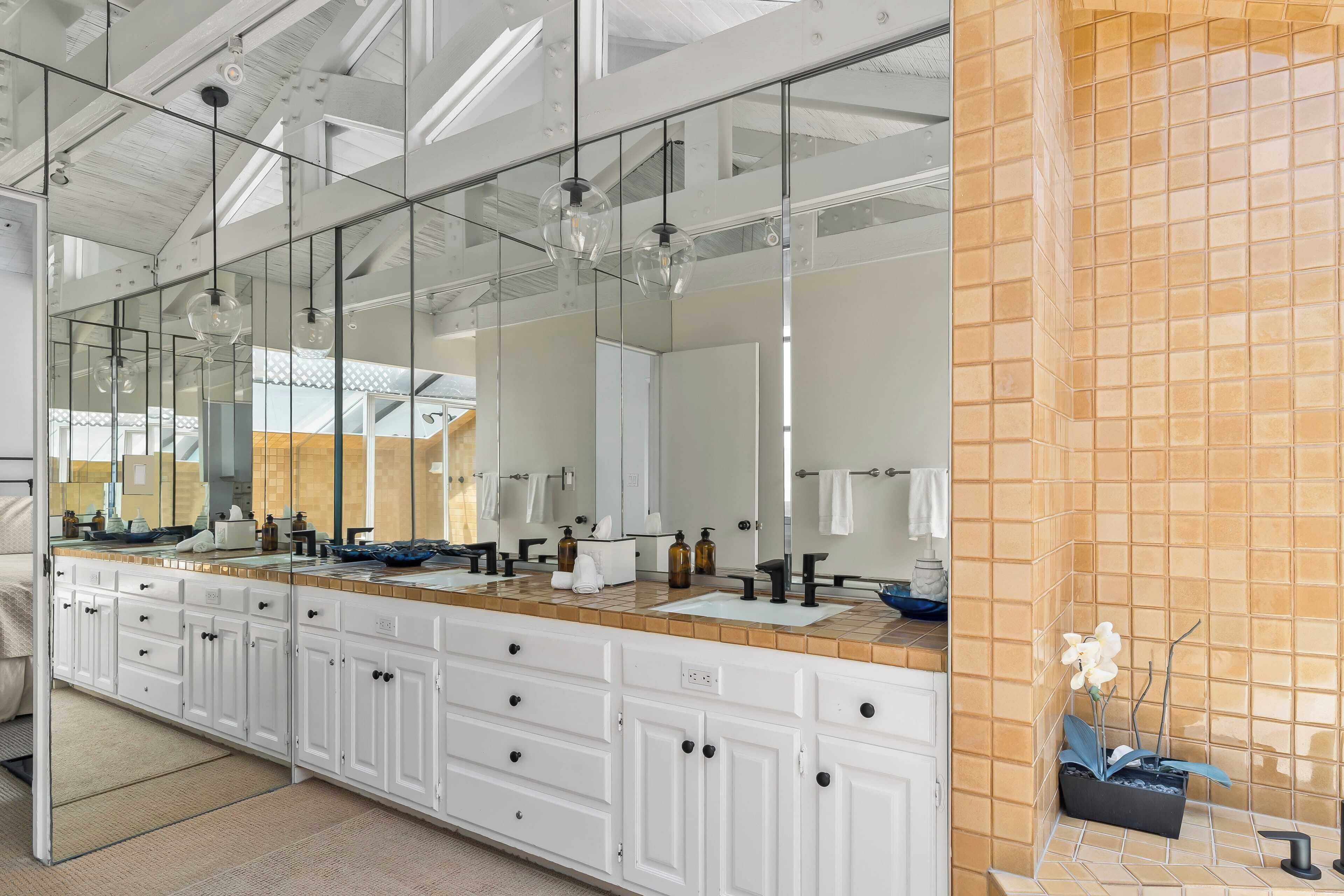 A modern bathroom with a large mirror, white cabinetry, and a tiled backsplash.