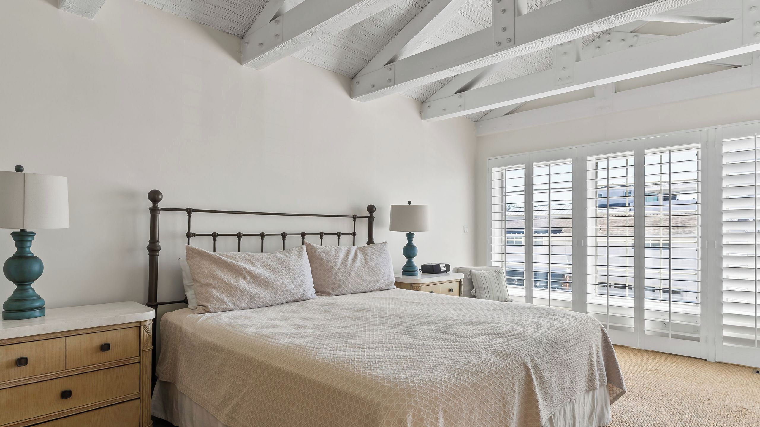 A bedroom with a bed, bedside tables, lamps, a window with blinds, and a view of the outside.