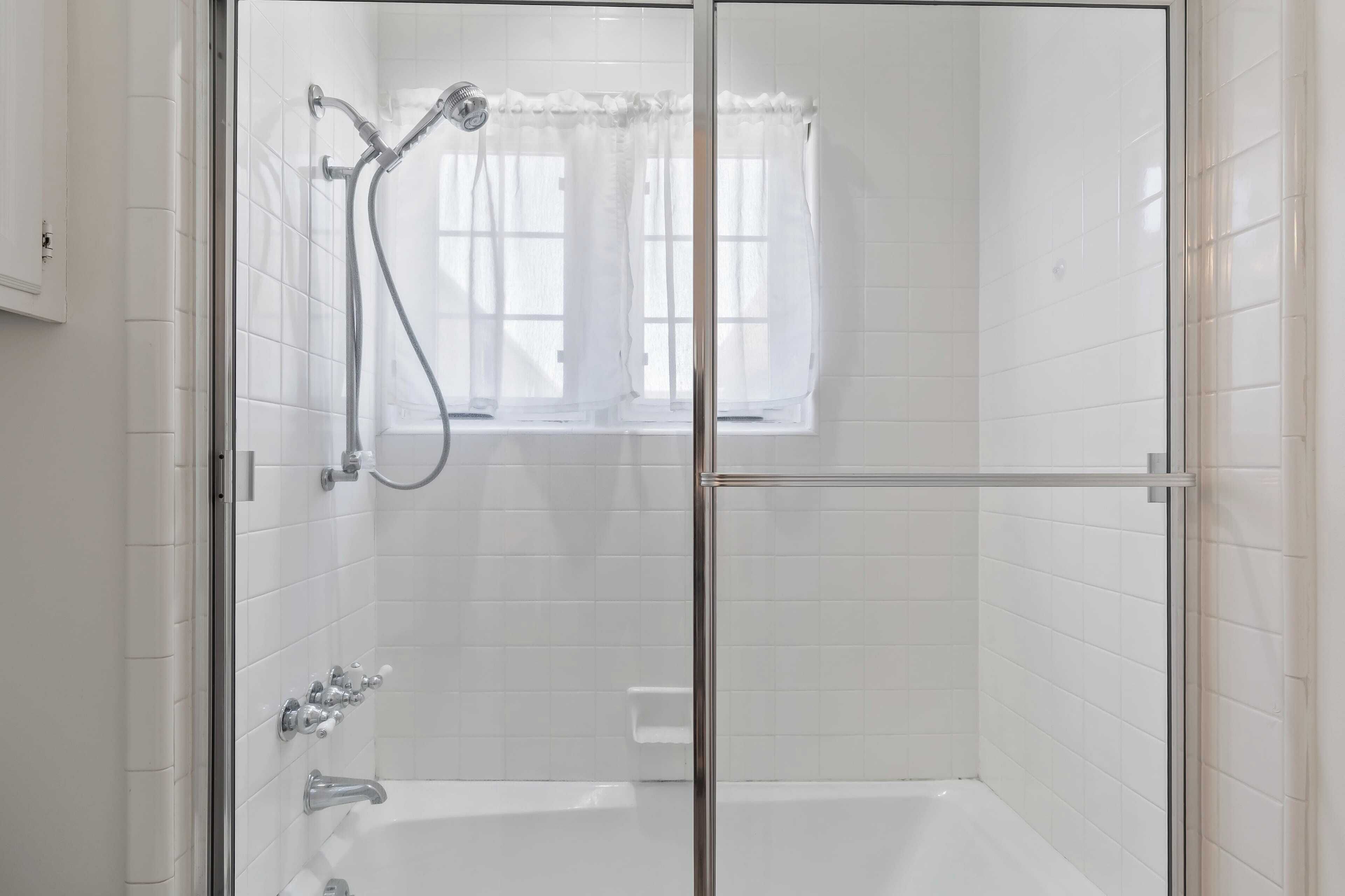 A glass-enclosed shower area with a window and a bathtub.
