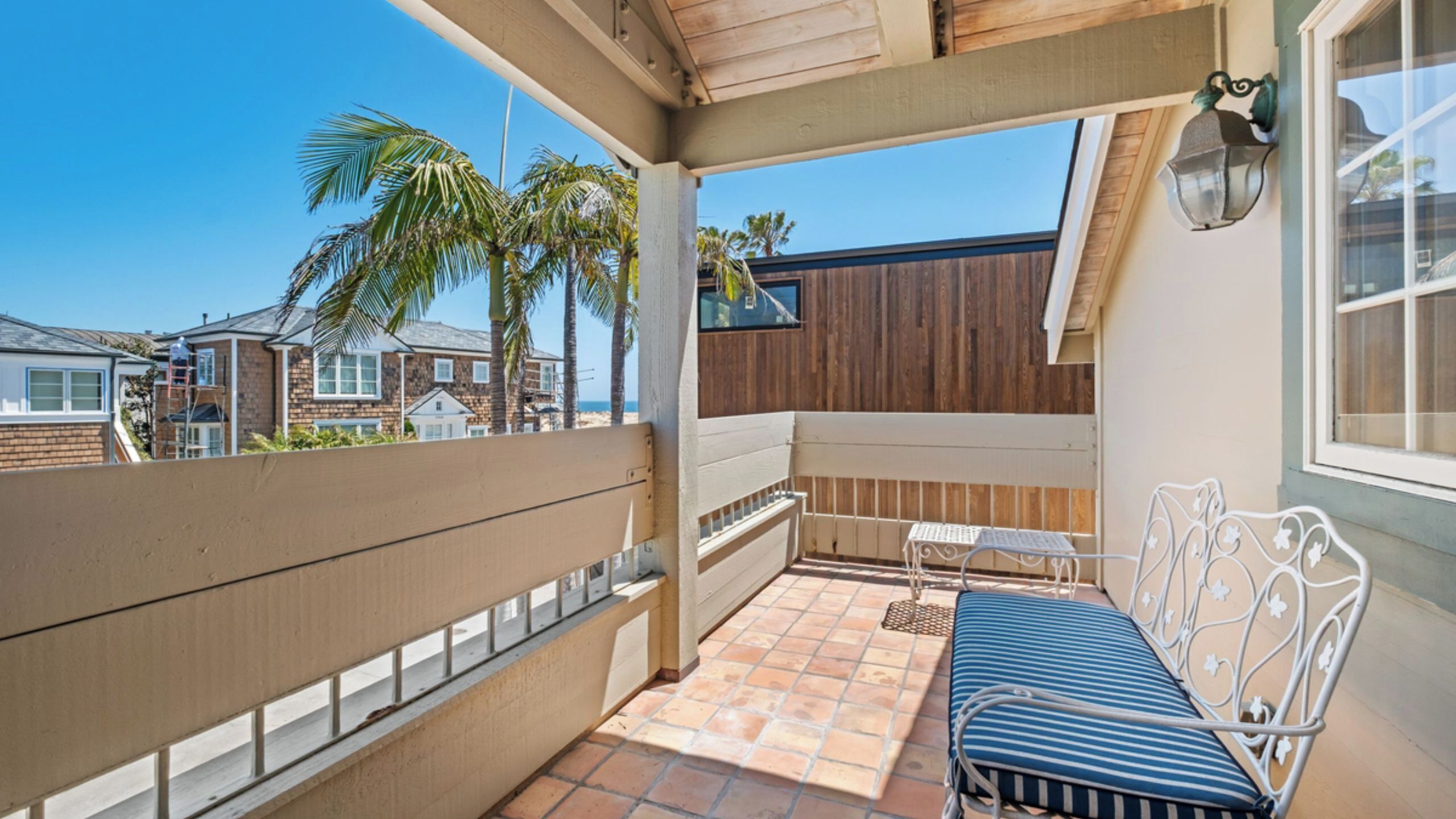 A covered balcony with a table and chairs, a view of palm trees, and a wooden fence.