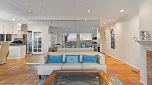 A spacious living room with a white sofa, a coffee table, and a view of the kitchen and dining area through glass doors. - Oceanfront Home Walk to Balboa Pier + Scenic Views Balboa Peninsula Point by Avantstay (Newport Beach)