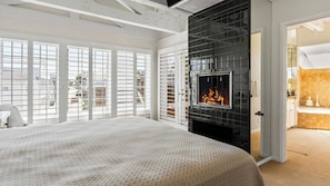 A bedroom with a fireplace, large windows, and a view of the outside. - Oceanfront Home Walk to Balboa Pier + Scenic Views Balboa Peninsula Point by Avantstay (Newport Beach)