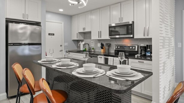 A modern kitchen with white cabinets, stainless steel appliances, and a central island with seating. - Cozy Orlando home close to parks, dining, and downtown fun (Orlando)
